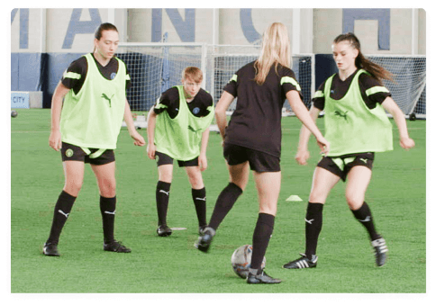 Group of 4 female footballers training on an indoor football pitch with CITYPLAY smart tracker attached to their football boots